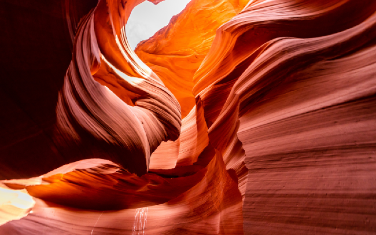 Interno dell'Antelope Canyon: le pareti di arenaria rossa e arancione scavate dall'acqua formano curve sinuose illuminate da un fascio di luce naturale che filtra dall'apertura in alto