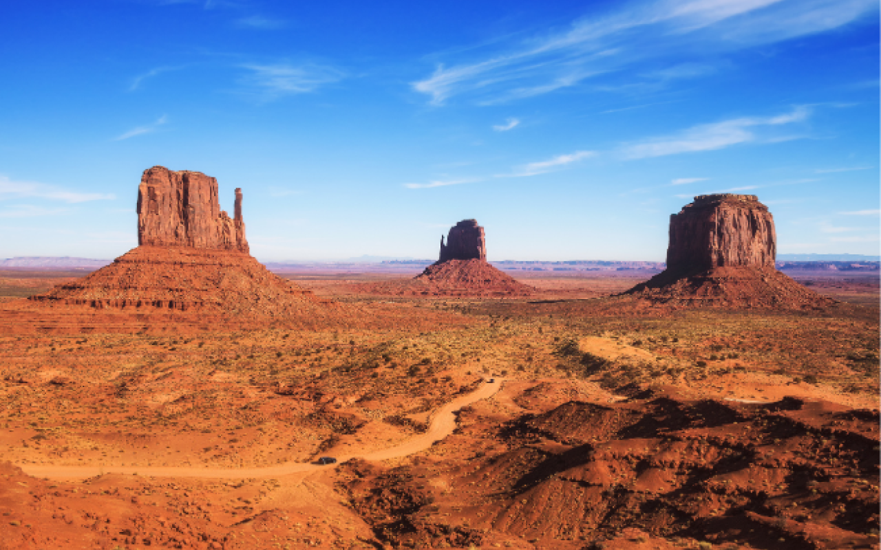 Le tre iconiche formazioni rocciose della Monument Valley — le Mittens e la Merrick Butte — si stagliano sulla sabbia rossa del parco tribale Navajo al confine tra Arizona e Utah sotto un cielo azzurro