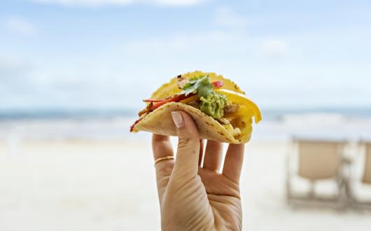foto di un tacos in mano davanti al mare in spiaggia a tulum (riviera maya,messico)