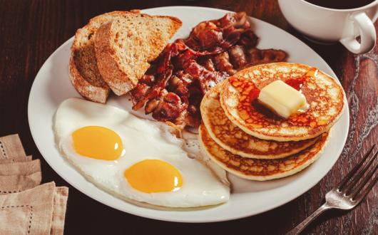 piatto a base di uova, pane tostato, bacon e pancakes