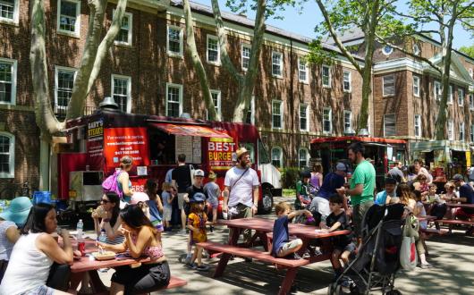 persone che mangiano ai tavoli dei food truck per strada