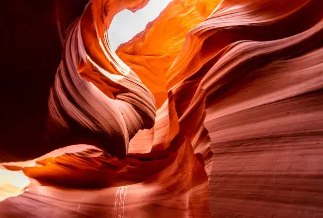 Interno dell'Antelope Canyon: le pareti di arenaria rossa e arancione scavate dall'acqua formano curve sinuose illuminate da un fascio di luce naturale che filtra dall'apertura in alto