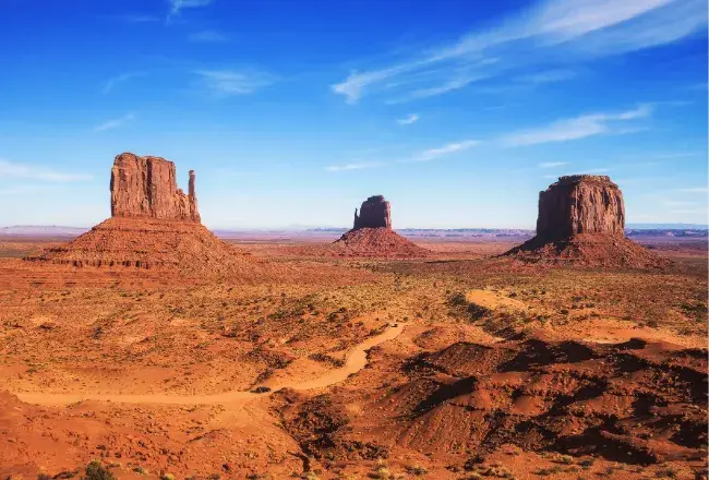 Le tre iconiche formazioni rocciose della Monument Valley — le Mittens e la Merrick Butte — si stagliano sulla sabbia rossa del parco tribale Navajo al confine tra Arizona e Utah sotto un cielo azzurro